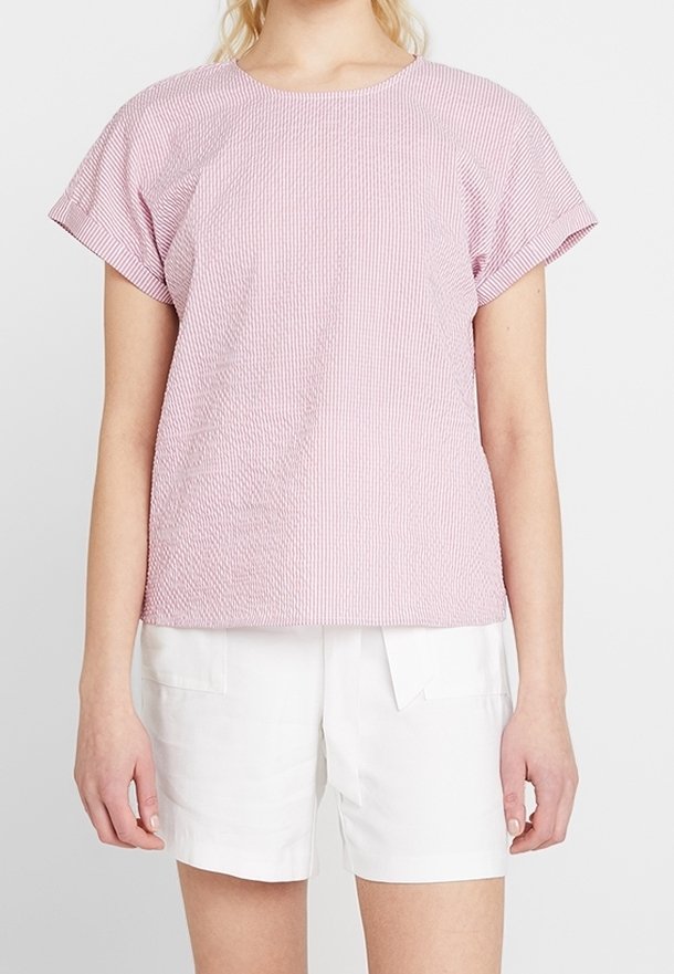 Blouse à manches courtes, rayée rose et blanche, avec un col rond et un tissu texturé. Associée à un short blanc plissé.