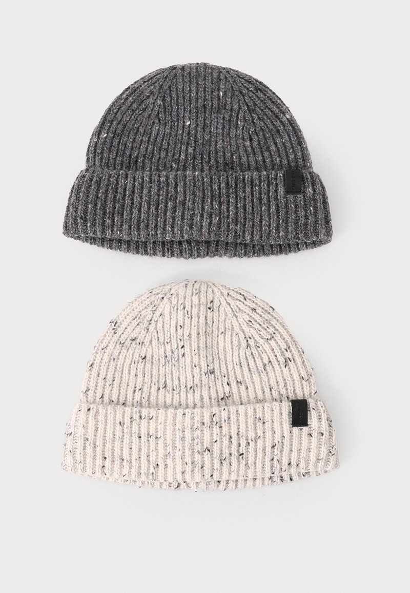Two knitted beanies: one dark gray with speckles, the other light cream with flecks. Both have a folded ribbed cuff and a small black tag.