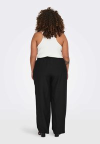 Μαύρο παντελόνι με φαρδιά πόδια και ελαστική μέση συνδυασμένο με λευκό αμάνικο τοπ, που δείχνει μια λεία υφή υφάσματος από την πίσω όψη.