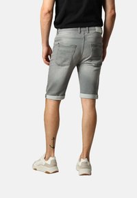 Shorts en denim gris avec des ourlets retournés, dotés de deux poches arrière et d'une coupe slim. Portés avec des baskets de couleur claire.