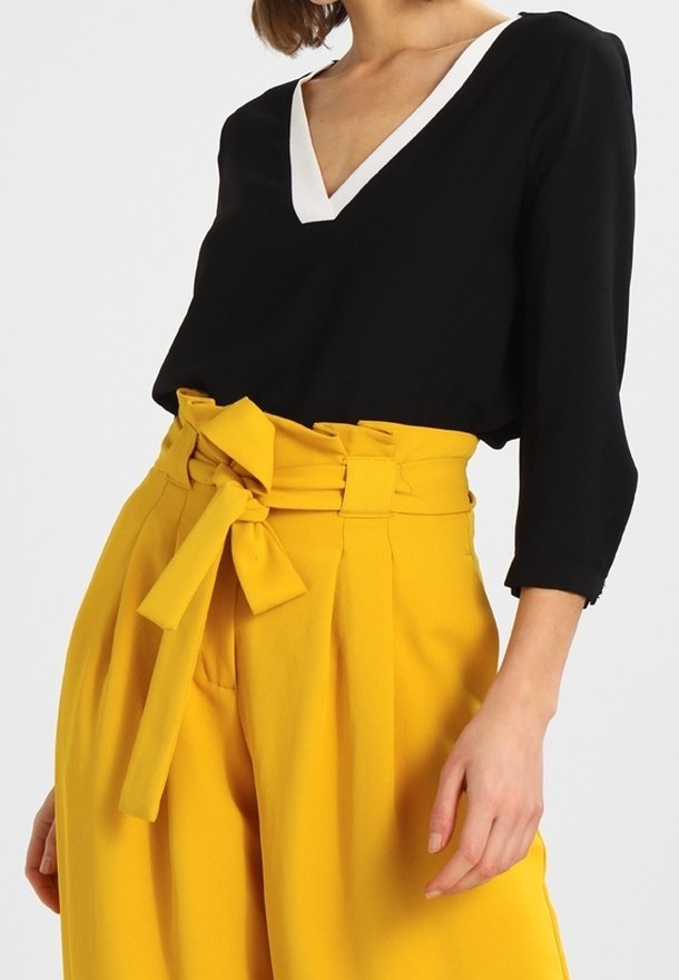 Blusa nera con scollatura a V bianca; abbinata a pantaloni gialli a vita alta con pieghe e un fiocco legato in vita.
