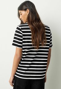 Črno-bela črtasta majica s kratkimi rokavi in sproščenim krojem. Ima okrogel izrez in gladko, mehko teksturo tkanine.