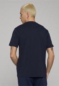 Tmavomodré bavlnené tričko s okrúhlym výstrihom, krátkymi rukávmi a rovnou lemem. Má viditeľné švy a hladkú textúru.