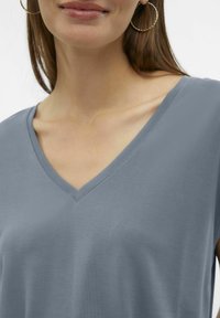 Top gris de manga corta con escote en V en tela suave. Tiene un corte relajado con costuras planas y una textura lisa. Diseño simple y minimalista.
