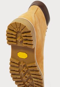 Barna velúr csizma vastag, strapabíró Vibram talppal és részletes profilmintázattal, alulnézetből, fehér háttér előtt.