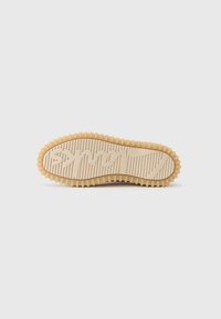 Rubber sneaker sole in beige with textured ridges and rounded edges. Features a prominent logo and grooves for traction.