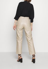 Beige läderbyxor med rak bendesign, med bakfickor och en slät yta, tillsammans med svarta högklackade sandaler med remmar.