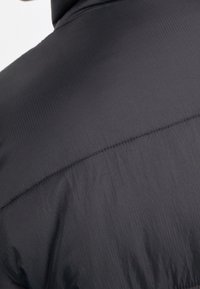 Czarna pikowana kurtka puchowa o fakturze pikowania, gładkim wykończeniu i wysokim kołnierzu, podkreślająca lekki materiał i ciepło.