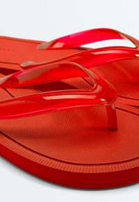 Paire de tongs rouges en caoutchouc avec semelle texturée et brides translucides brillantes, présentées en gros plan sur fond blanc.