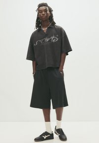 Black oversized T-shirt with a graphic design, paired with black knee-length shorts and black shoes, featuring white socks. Simple, casual look.