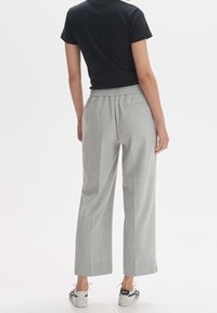 Pantalons plissés gris avec une taille élastique, des poches latérales et une coupe décontractée, associés à un haut noir à manches courtes et des baskets grises.