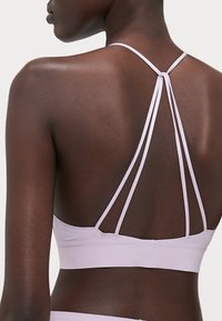 Soutien-gorge de sport violet clair avec de fines bretelles croisées au dos. Tissu lisse et extensible avec une finition soignée, conçu pour le confort et le soutien.