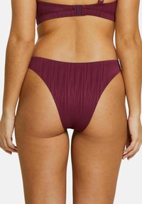 Bas de bikini bordeaux avec un motif texturé, ouvertures de jambe haute et couverture minimale. Le détail de couture le long des bords améliore le design.