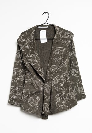 Mørkegrå cardigan med blomsterprint, åben foran og med lange ærmer, hænger på en sort bøjle mod en hvid baggrund.