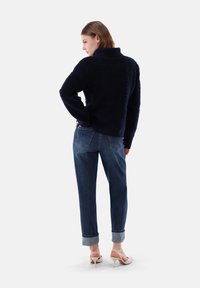 Marineblauer, bequemer Pullover mit hohem Kragen, strukturiertem Stoff, kombiniert mit hochgekrempelten blauen Jeans und hellen Schuhen.