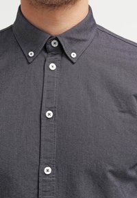 Chemise gris foncé à boutons avec col pointu, accents de boutons blancs et texture subtile avec une patte de boutonnage avant élégante.