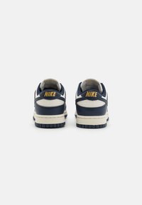 Navy leather sneakers with cream accents, featuring a gold Nike logo on the heel and a textured rubber sole. Designed in a low-top silhouette.
