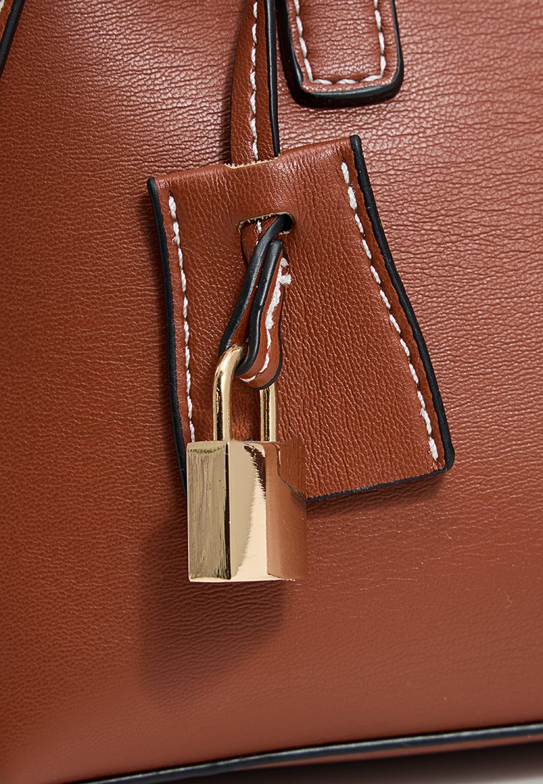 Sac à main en cuir marron avec des coutures blanches contrastantes, doté d'un cadenas en or et d'une étiquette rectangulaire en cuir attachée. Texture lisse.