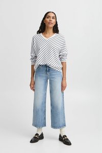 Gestreifter, leichter Pullover in Weiß und Marineblau, kombiniert mit weit geschnittenen hellblauen Jeans. Das Model trägt schwarze Slipper und weiße Socken.