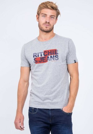 T-shirt gris à manches courtes avec un imprimé graphique en rouge et bleu marine, col rond et coupe ajustée. Porté avec un jean bleu foncé.