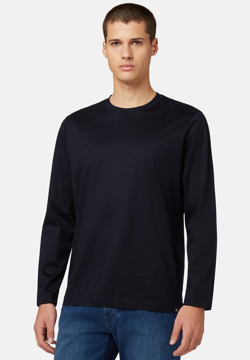 T-shirt en coton noir à manches longues avec un col rond, texture lisse et design minimal. Associé à un jean en denim bleu.