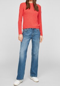 Pull en tricot rouge à manches longues, col rond et poignets côtelés. Assorti avec un jean large bleu clair et des baskets blanches.