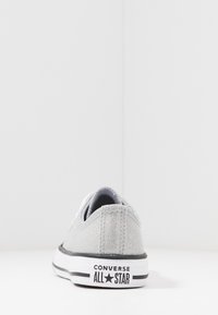 Silberne Glitzer-Leinenschuhe mit einem flachen Profil, weißer Gummi-Sohle, schwarzem Streifen und schwarzem "Converse All Star"-Logo an der Ferse.