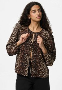 Blusa a stampa leopardata con scollo rotondo, maniche a sbuffo, chiusura frontale con fiocco e dettagli neri. Realizzata in tessuto morbido con texture variate.