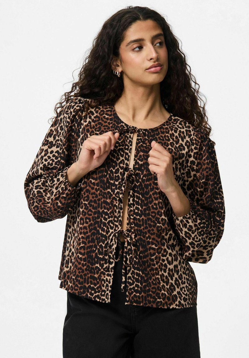 Blusa a stampa leopardata con scollo rotondo, maniche a sbuffo, chiusura frontale con fiocco e dettagli neri. Realizzata in tessuto morbido con texture variate.