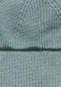 Berretto lavorato a maglia in un morbido e leggero teal chiaro. Pattern a coste testurizzato con bordo ripiegato. Il materiale appare caldo e accogliente.