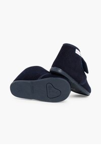 Pantofole in corduroy blu navy con punta arrotondata, chiusura con cinturino in Velcro e suola in gomma testurizzata con un design a forma di cuore sul fondo.