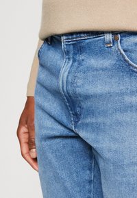 Světle modré džíny z denimu s klasickým pětikapsovým designem, jemným vyblednutím a švy podél švů.