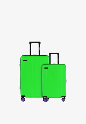 Twee koffers in levendig groen, één groter met zwarte sluitingen, verticale groeven en paarse accenten, gemonteerd op vier wielen voor gemakkelijke manoeuvreerbaarheid.