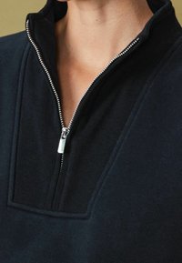 Navy blue pullover with a zippered collar. Features a textured collar area, smooth body fabric, and metallic zipper detail.