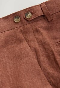 Pantalons en lin marron avec une surface texturée, fermeture à double bouton et poches latérales, au fit ajusté.