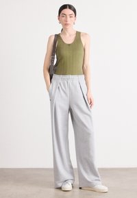 Olivengrønn ribbet tanktop med høy hals, kombinert med lysegrå vide joggebukser. Outfiten har frontfolder og en avslappet passform.