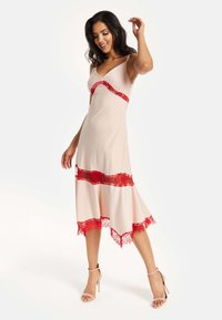 Knee-length, beige dress with delicate red lace accents. Features thin straps, a V-neck, and a flowing hemline. Smooth texture.