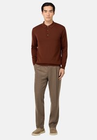 Ruda ilga rankovė polo marškiniai su apykakle ir mygtukų eiliu, derinami su šviesiai rudomis dryžuotomis kelnėmis ir kreminės spalvos slip-on bateliais.