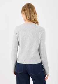 Gai pelēks adīts džemperis ar ribotu apakšmalu un garām piedurknēm, kas piedāvā apaļu kaklu un raglāna plecus. Sīki redzama auduma tekstūra.