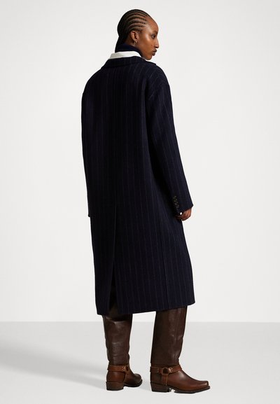 Jūras spēku pinstripes mētelis ar garu siluetu, sānu atveri un iegriezto apkakli, apvienots ar brūnām ādas nūjām līdz ceļiem un potīšu atsaitēm.