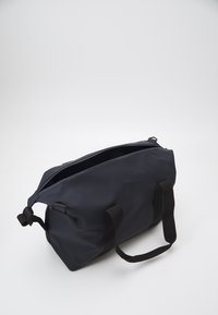 Σκούρα μπλε τσάντα duffel από αδιάβροχο υλικό, με μαύρες υφασμάτινες λαβές και φερμουάρ, με μινιμαλιστικό σχέδιο.