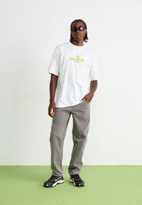 Hvid oversized t-shirt med farverigt grafisk logo, grå løse bukser og sorte athletic sko med hvide accenter.