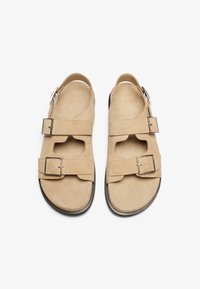 Sandales en daim beige avec deux sangles ajustables et boucles en argent ; conception à bout ouvert et talon découvert ; semelle intérieure texturée pour le confort.