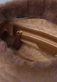 Interno di una borsa foderata in pelliccia marrone, caratterizzato da un tessuto beige con logo in rilievo, tasca con zip e accessori in metallo dorato.