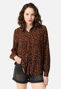 Brun leopardtryckt skjorta med knappar och långa ärmar, med en avslappnad passform och klassisk krage, tillsammans med mörk denimshorts.