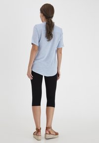 Jasnoniebieska koszula z krótkim rękawem o luźnym kroju, zestawiona z czarnymi legginsami capri i beżowymi sandałami na koturnie, prezentująca swobodny strój.