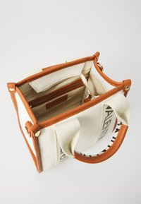 Saco de lona com detalhes em pele castanha, vista aberta mostrando o bolso interior, forro creme e o nome da marca impresso de lado.