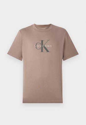 T-shirt en coton marron clair à manches courtes avec le logo "CK Calvin Klein" imprimé en noir et blanc sur la poitrine, présenté sur un fond uni.