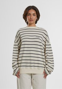 Maglione a righe in crema con linee navy, con scollo a giro e vestibilità over. Tessuto testurizzato con polsini e orlo a costine.