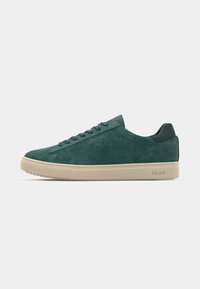 Green suede sneakers with a low-profile design, featuring a beige rubber sole and matching laces. Branding on the heel.